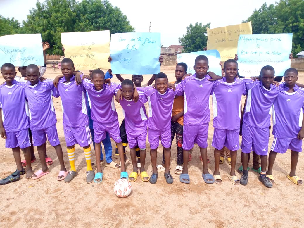 Children in purple football uniforms standing together beside a football